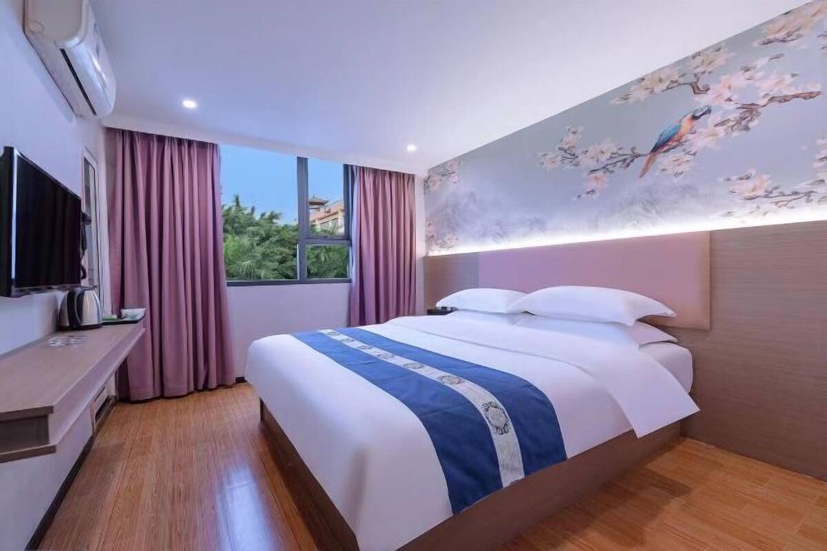 A hotel room with a bed, a TV, a desk, and a window with curtains.
