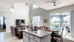 A spacious kitchen with a large island, a dining area with a table and chairs, a sofa, and a TV. - Spacious Getaway with Pool on stunning Golf Course (Haines City)