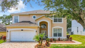 A two-story house with a garage, a front entrance with a covered porch, and a landscaped front yard with various plants. - Spacious Getaway with Pool on stunning Golf Course (Haines City)