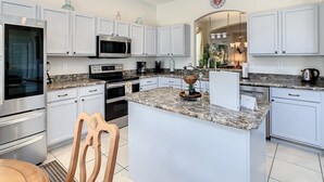 A modern kitchen with white cabinetry, stainless steel appliances, granite countertops, and a central island. - Spacious Getaway with Pool on stunning Golf Course (Haines City)