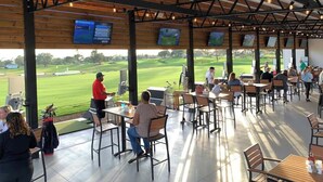 A covered outdoor dining area with tables and chairs, overlooking a golf course. - Spacious Getaway with Pool on stunning Golf Course (Haines City)