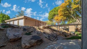A modern building with a stone pathway, a staircase leading to a covered area, and a large rock formation. - Pet-Friendly Condo with Private Hot Tub & Views (St. George)