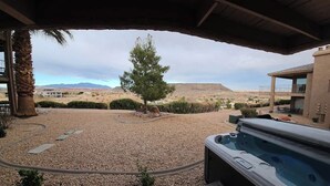 A covered outdoor area with a hot tub, gravel ground, and a view of a desert landscape. - Pet-Friendly Condo with Private Hot Tub & Views (St. George)