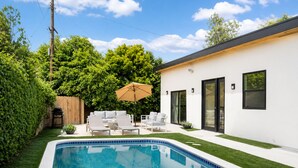 A swimming pool with a tiled edge, a white building with black-framed windows, and a wooden fence.