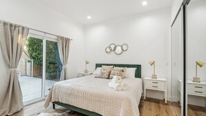 A bedroom with a bed, a nightstand, a mirror, and a view of the outdoors.