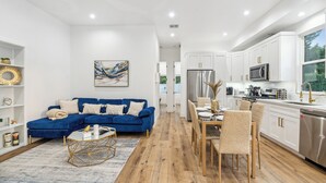 A modern kitchen with white cabinets, stainless steel appliances, and a dining area with a blue sofa and wooden chairs.