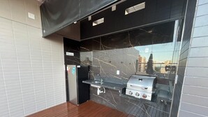 A modern outdoor kitchen area with a grill, a sink, and a tiled backsplash.
