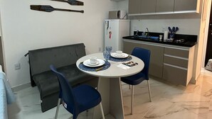 A compact kitchen with modern appliances, a dining area with a round table and blue chairs, and a grey sofa.