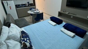 A hotel room with a bed, a TV, a small kitchen area, and a dining table.