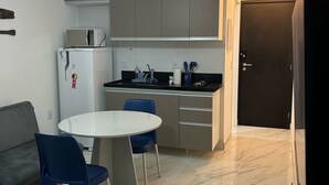 A compact kitchen with modern appliances, a dining area with a round table and blue chairs, and a door leading to another room.