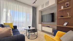 Ein modernes Wohnzimmer mit einer Couch, einem gelben Sessel, einem Couchtisch und einem an der Wand befestigten Flachbildfernseher.