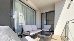 Ein moderner Balkon mit weißen Möbeln, darunter eine Sitzecke mit Sofa und Stühlen sowie ein Glastisch.