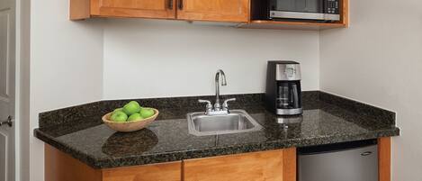 A compact kitchen with a granite countertop, a stainless steel sink, a microwave, and a coffee maker.