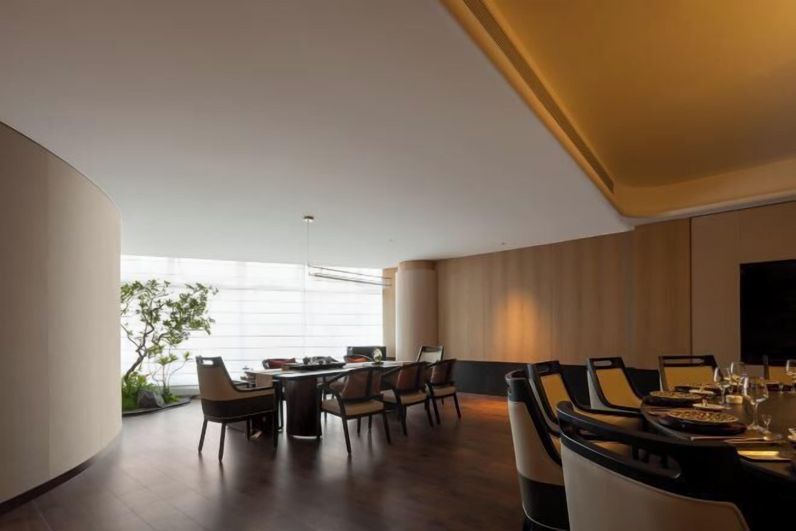 Uma sala de jantar moderna com uma mesa redonda, várias cadeiras e uma grande janela que ilumina naturalmente o espaço.