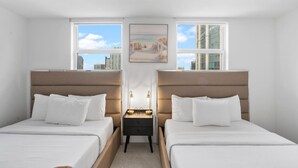 A hotel room with two beds, a small table with lamps, and large windows offering a city view.