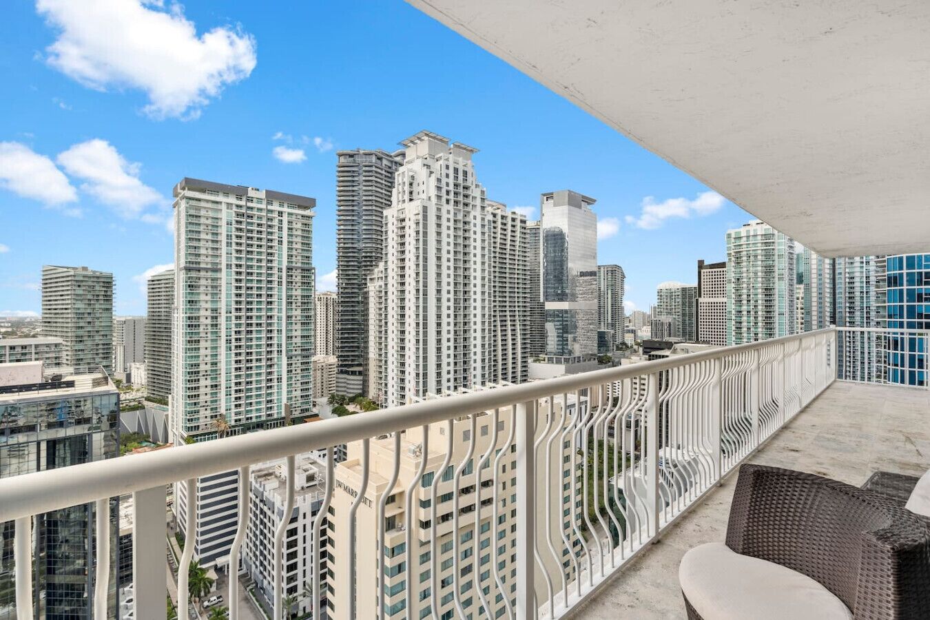 Un balcón con vistas a edificios altos, una barandilla y mobiliario exterior.