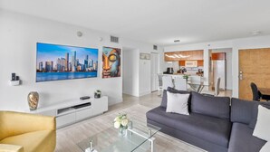 A modern living room with a grey sofa, a glass coffee table, and a cityscape painting on the wall.