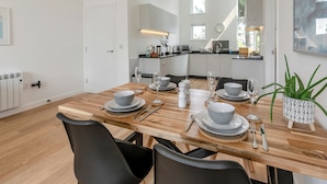 Una cocina moderna con armarios blancos, una mesa de comedor de madera dispuesta con platos, vasos y cubiertos, y una planta en maceta sobre la mesa.