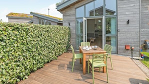 Una casa moderna con terraza, una mesa de comedor con sillas y un ventanal grande.