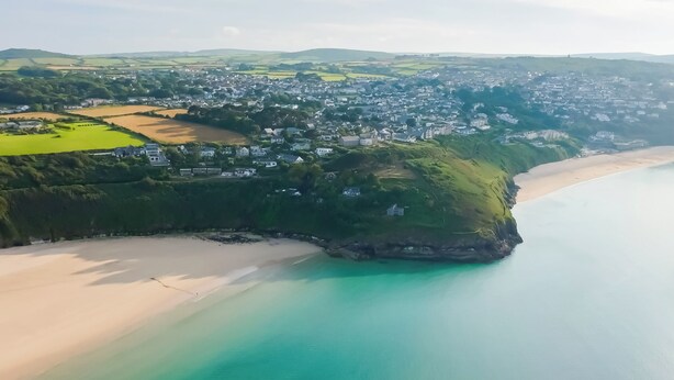 Vista aérea de un pueblo costero con playa, casas y vegetación.
