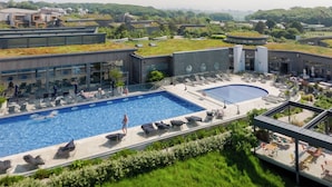 Un hotel moderno con una amplia piscina exterior, tumbonas y una terraza en la azotea.