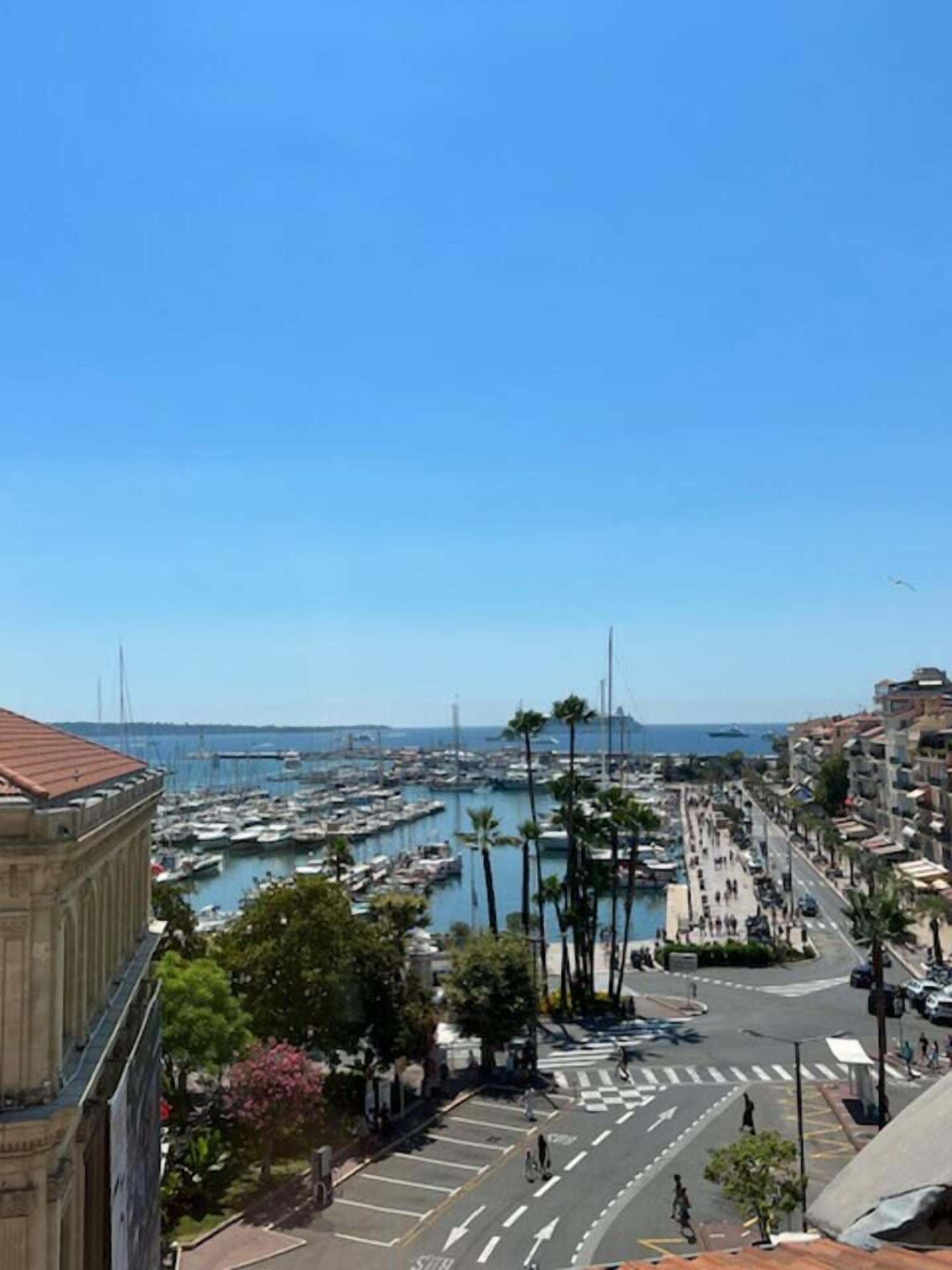 Paesaggio costiero con un porto turistico, edifici storici e un cielo azzurro limpido.