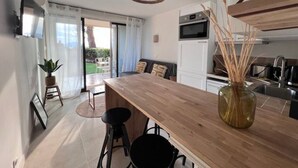 A modern kitchen with a wooden island, a dining area with a table and chairs, and a large window with curtains. - Apartment for 4 with sea view, pool, and pkg (Cannes)