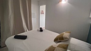 A hotel room with a bed, a wall-mounted light, and a door with a towel rack. - Apartment for 4 with sea view, pool, and pkg (Cannes)