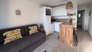 A modern kitchen with white cabinets, a wooden island, and a dark gray sofa with patterned cushions. - Apartment for 4 with sea view, pool, and pkg (Cannes)