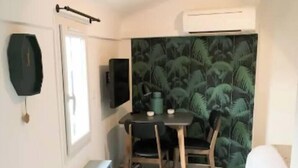 Une pièce de taille modeste comprenant un lit, une petite table avec des chaises, un téléviseur et un mur orné d’un motif vert.