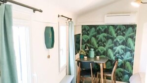Une pièce avec un plancher en bois, une table à manger avec des chaises, un petit escalier et un mur orné d’un motif de feuilles tropicales.