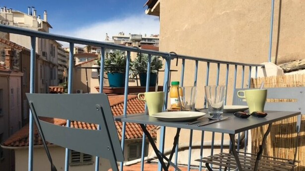 Un balcon avec une table dressée pour deux personnes, des plantes en pot et une bouteille d’eau.