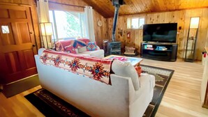 Interior acogedor de una cabaña con sofá, chimenea, televisión y paredes de madera.