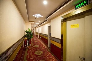 A hotel hallway with a red carpet, a potted plant, and a door with a 'No Smoking' sign.