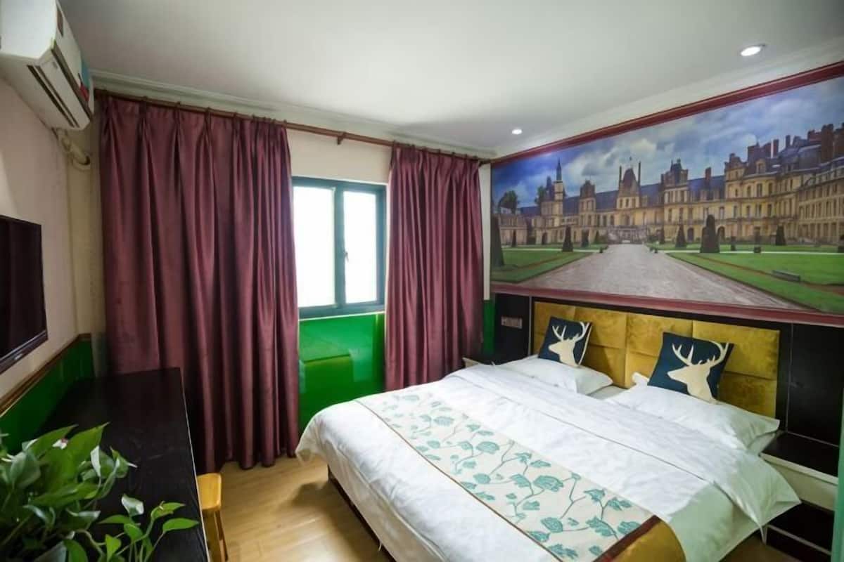 Una habitación de hotel con cama, cortinas, un cuadro, televisor y planta.