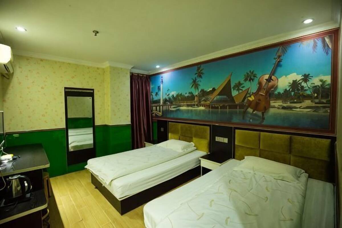 Habitación de hotel con dos camas, un escritorio, un espejo y un mural con una playa.