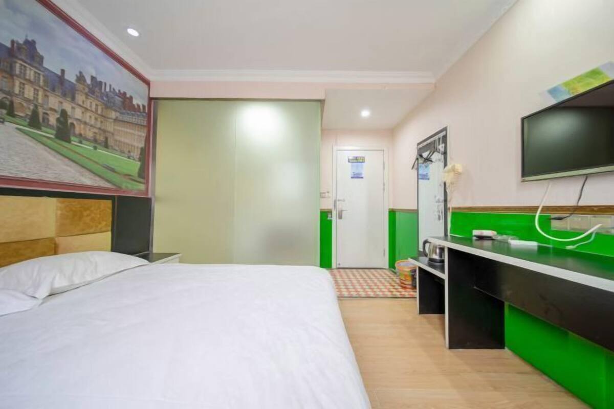 Una habitación de hotel con una cama, un escritorio con computadora, un televisor y un cuadro en la pared.
