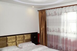 A hotel room with a bed, a headboard, a window with curtains, and a wall-mounted speaker. - Jinshang Hostel (Shanghai)