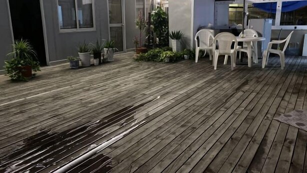 An outdoor patio area with wooden flooring, white plastic chairs, and potted plants.