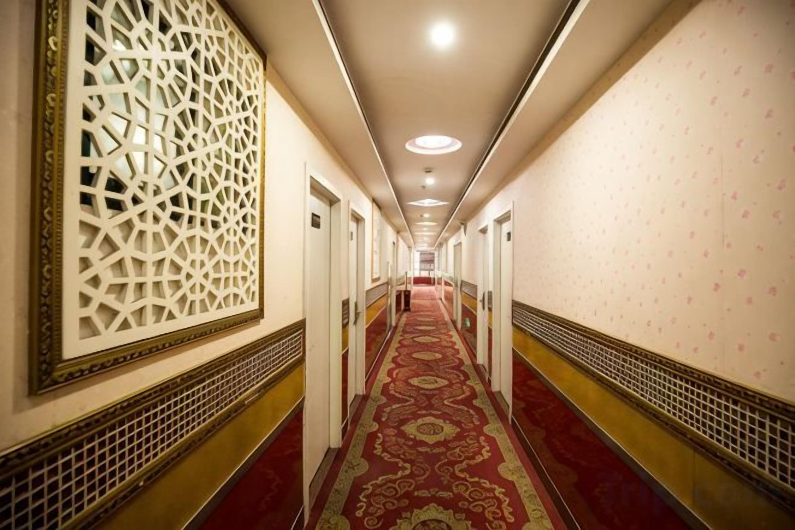 A long hallway with patterned walls and a red carpet, leading to a door at the end.