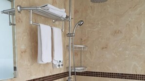 A bathroom with a shower, a towel rack with towels, and a tiled floor.