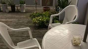 Un patio con dos sillas de plástico blanco y una mesa redonda, rodeado de plantas en macetas.