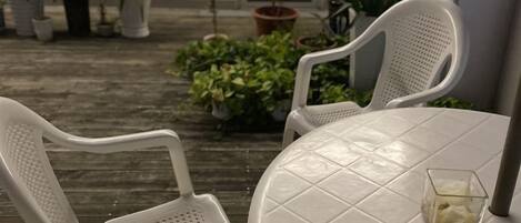 A patio with two white plastic chairs and a round table, surrounded by potted plants.