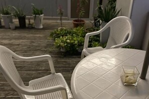 A patio with two white plastic chairs and a round table, surrounded by potted plants. - Jinshang Hostel (Shanghai)