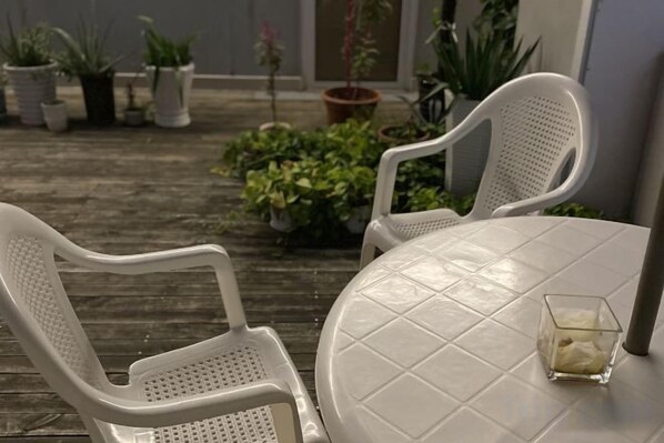A patio with two white plastic chairs and a round table, surrounded by potted plants.