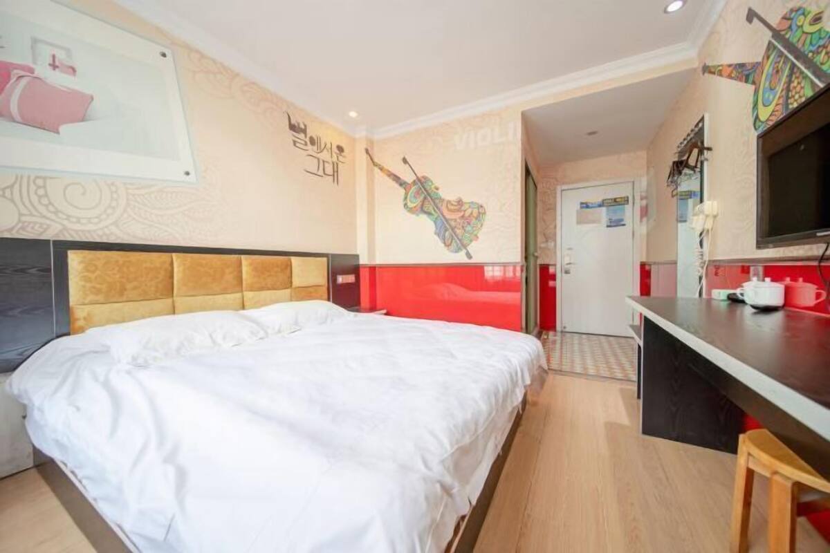 Una habitación de hotel con una cama, un escritorio, un televisor y un mural de un violín en la pared.