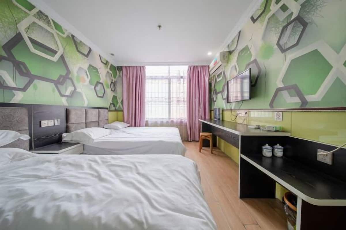 Una habitación de hotel con dos camas, televisión, escritorio y ventana con cortinas.