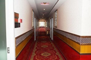 A hotel corridor with a red carpet, white walls, and a tiled border.