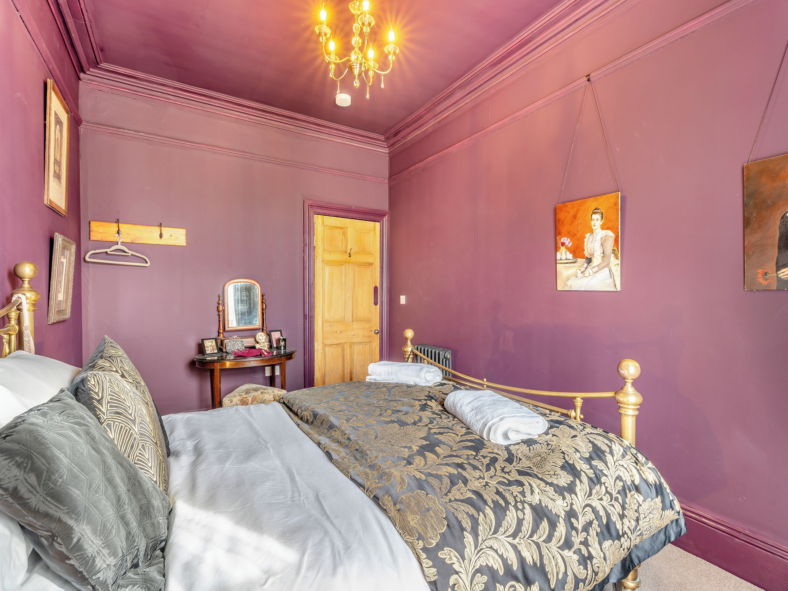 A bedroom with a bed, a dresser, a mirror, a door, and a chandelier.