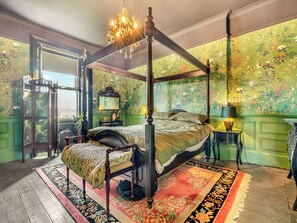 A four-poster bed with a canopy, a green floral wallpaper, and a red and black patterned rug.